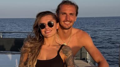 Sophia Thomalla (links) und Alexander Zverev sitzen auf einem Boot und lächeln in die Kamera.