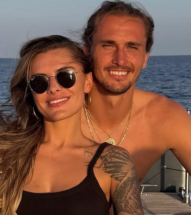 Sophia Thomalla (links) und Alexander Zverev sitzen auf einem Boot und lächeln in die Kamera.