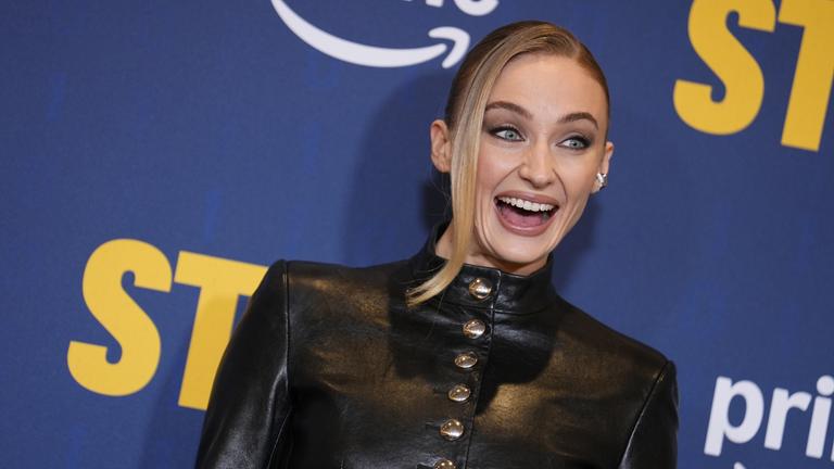 Schauspielerin Sophie Turner posiert bei einem Event vor einer Leinwand mit Sponsoren-Logos.