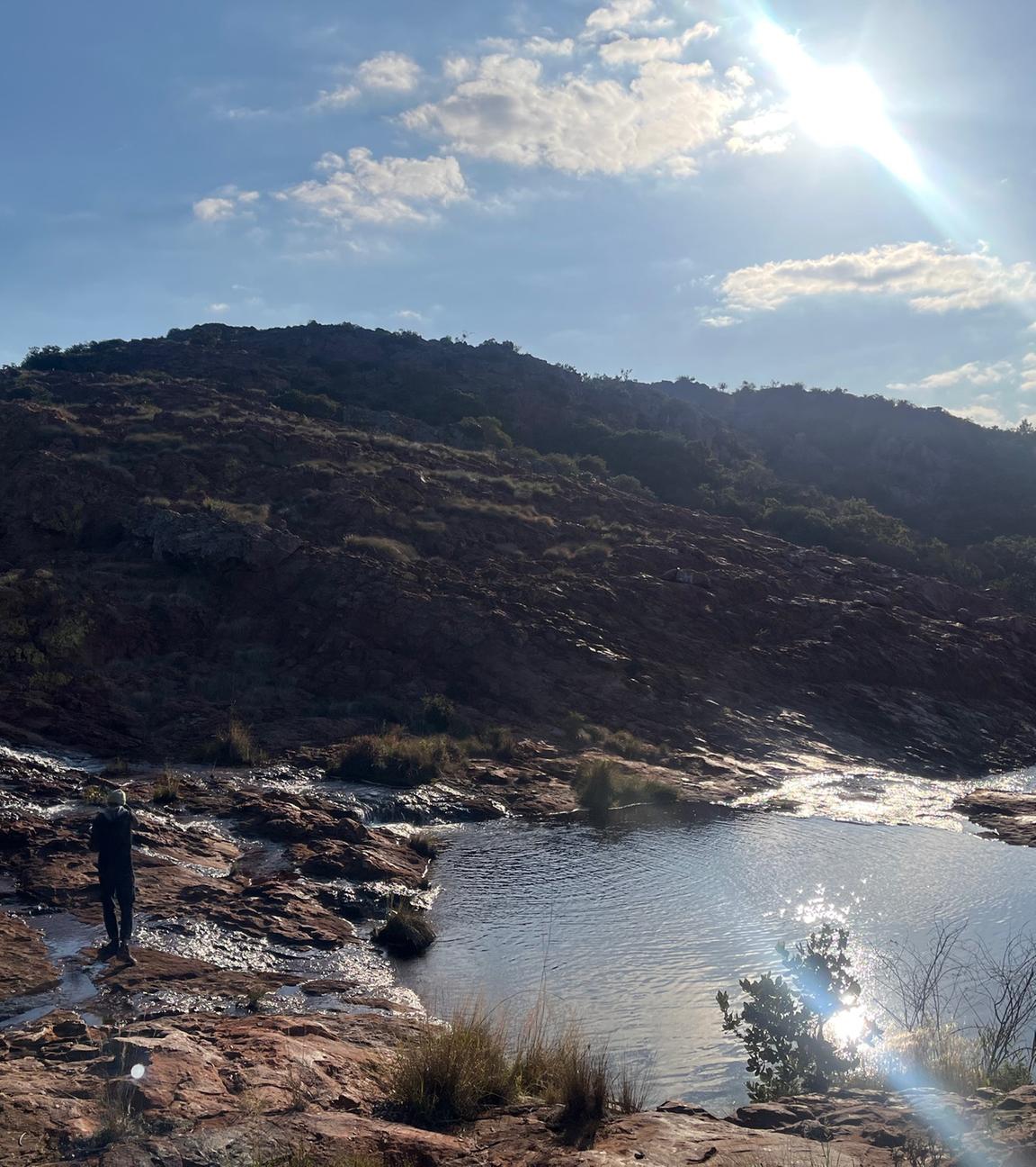 Eine Person steht an einem kleinen See vor dem Soutpansberg.
