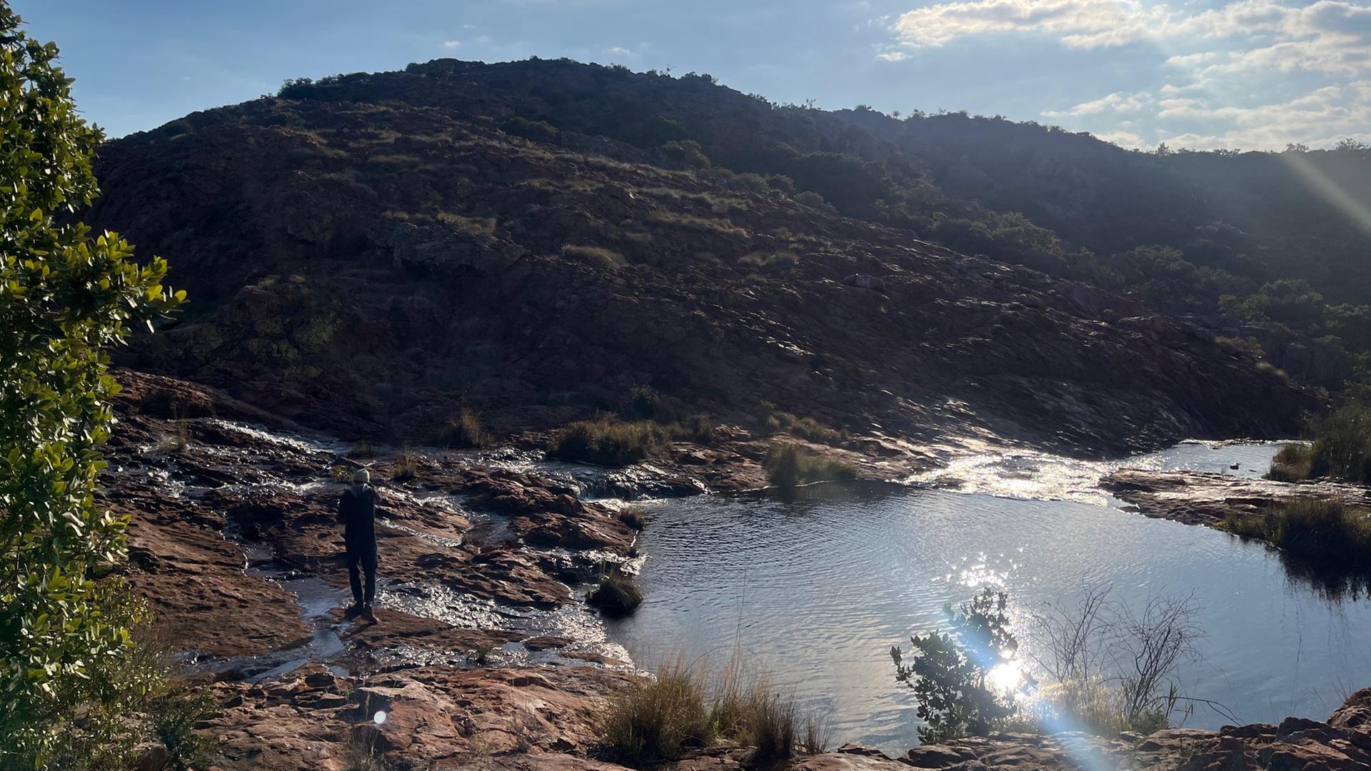 Eine Person steht an einem kleinen See vor dem Soutpansberg.