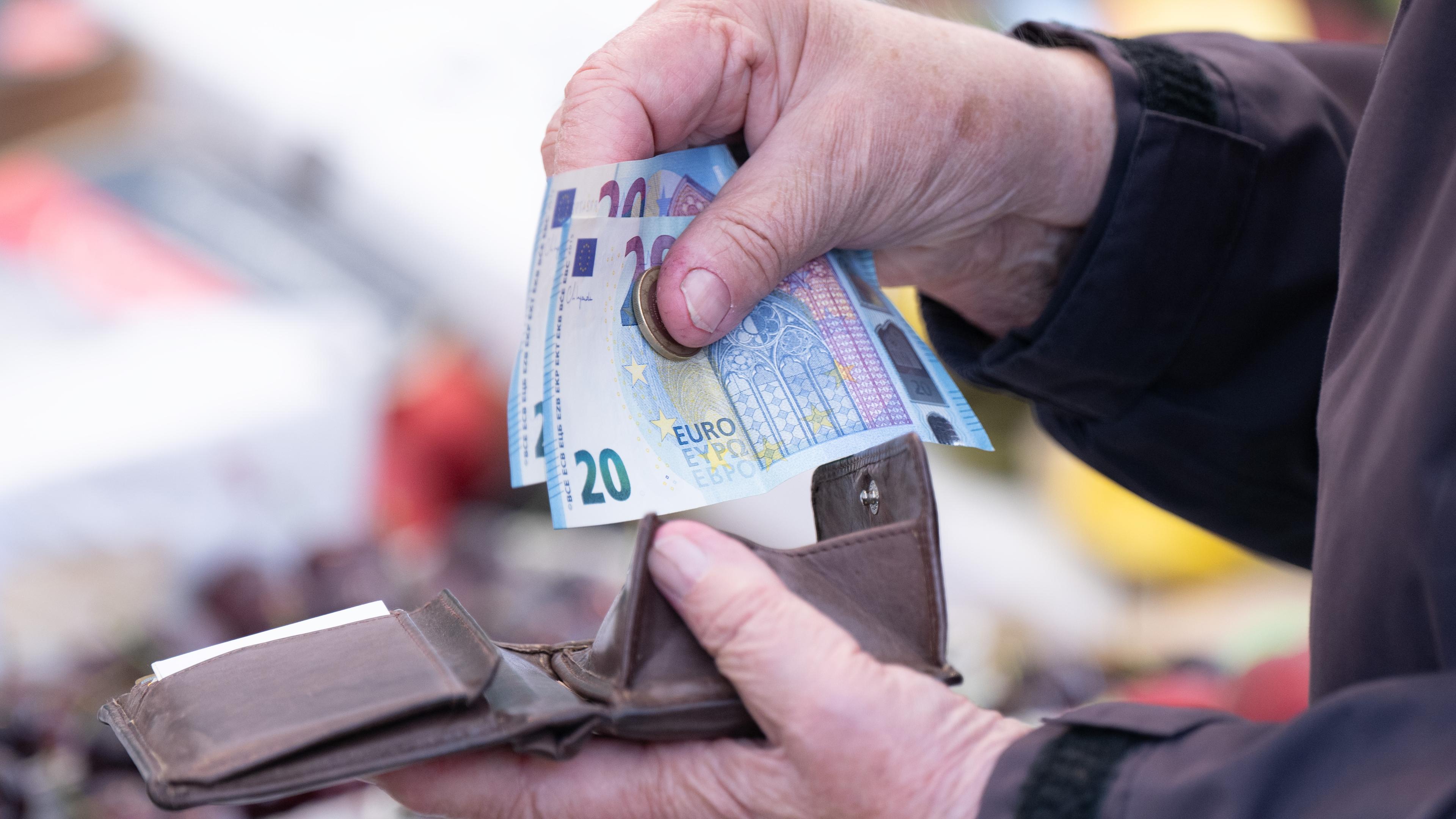 Eine Hand hält zwei 20-Euro-Scheine über einem Portemonnaie.