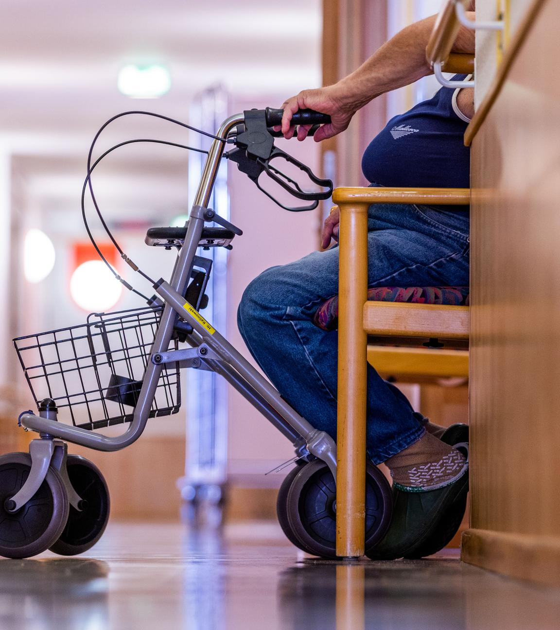  Ein Bewohner sitzt mit seinem Rollator auf einem Flur in einem Pflegeheim.
