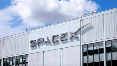 SpaceX-Logo an einem Gebäude, dahinter blauer Himmel mit einer Wolke.