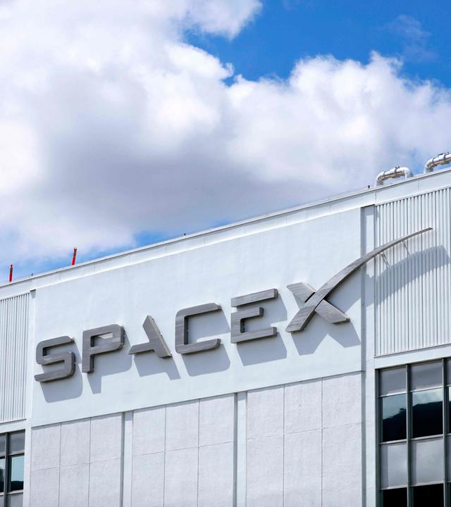 SpaceX-Logo an einem Gebäude, dahinter blauer Himmel mit einer Wolke.