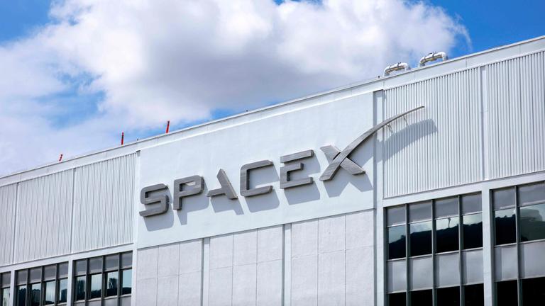 SpaceX-Logo an einem Gebäude, dahinter blauer Himmel mit einer Wolke.