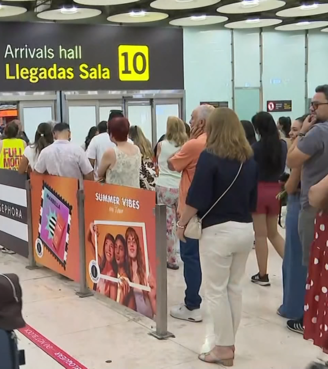 Reisende stehen und laufen in der Wartehalle eines spanischen Flughafens.