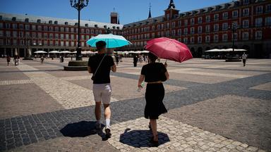 Zwei Personen laufen mit Schirmen durch Madrids Stadtmitte.