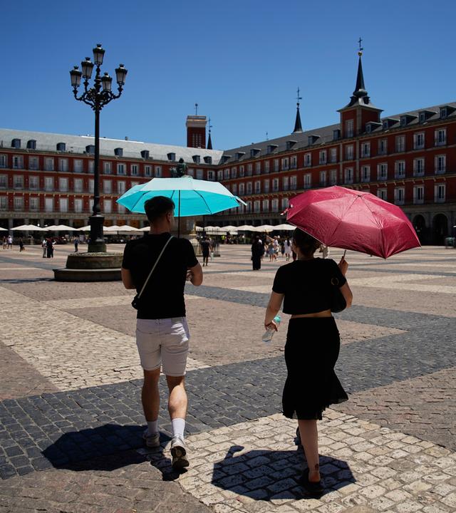 Zwei Personen laufen mit Schirmen durch Madrids Stadtmitte.