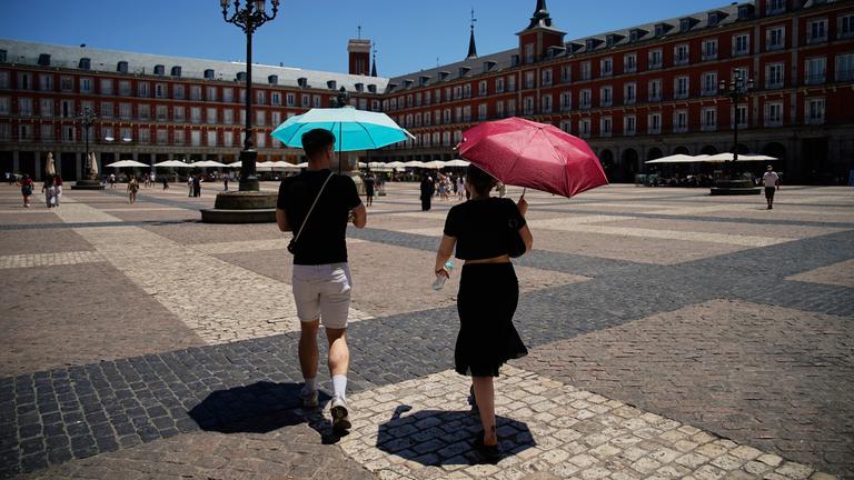 Zwei Personen laufen mit Schirmen durch Madrids Stadtmitte.