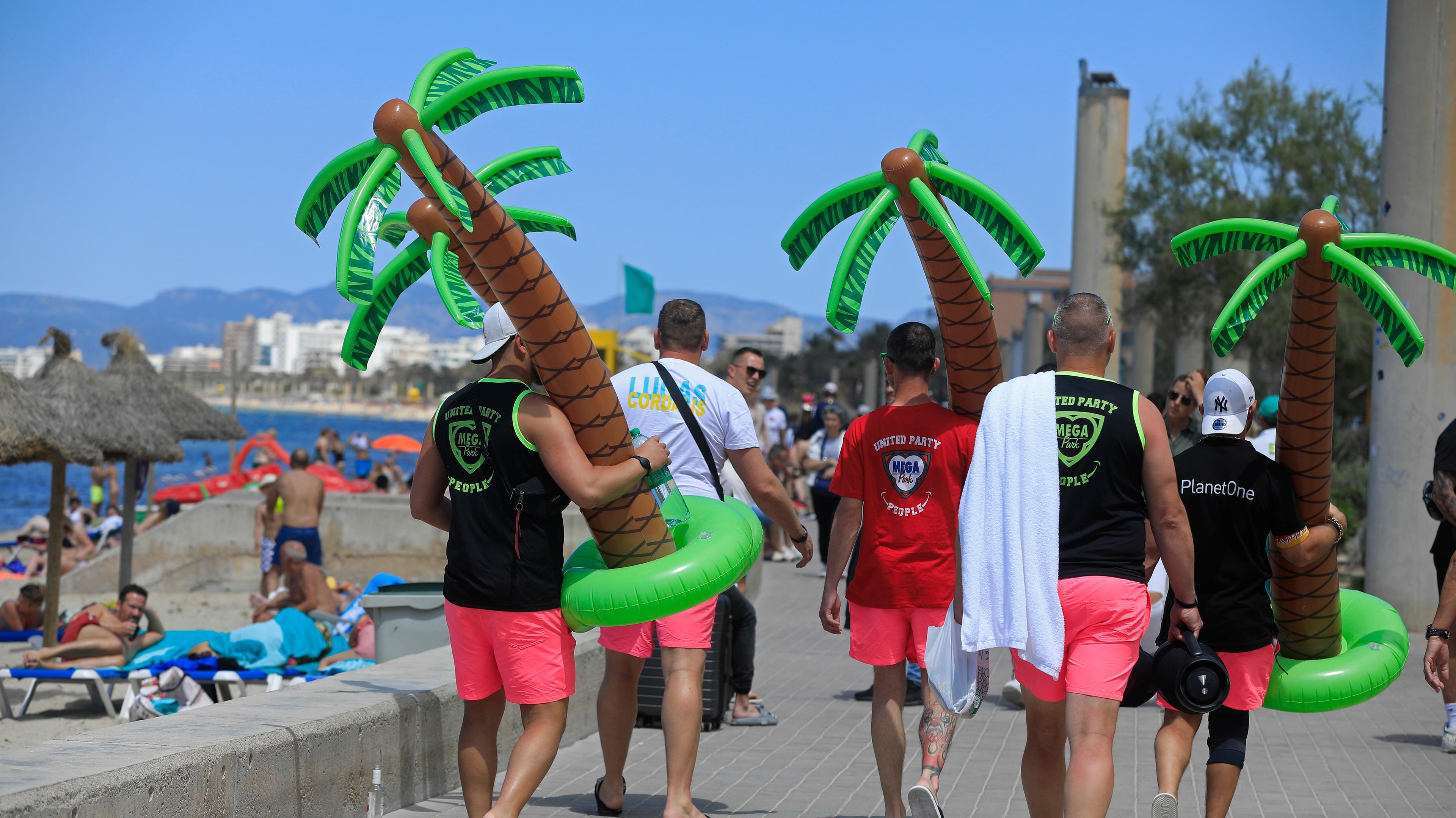 Spanien, Palma: Männer tragen an einem sonnigen Tag Plastikpalmen am Strand Arenal. Archivbild