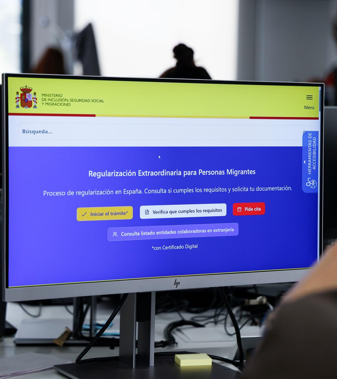 Ein junger Mann mit Ohrring schaut auf einen Computer. Darauf ist das gelb-blaue Online-Portal der spanischen Regierung zu sehen, über welches Migranten einen Aufenthaltstitel und eine Arbeitsgenemigung beantragen können.