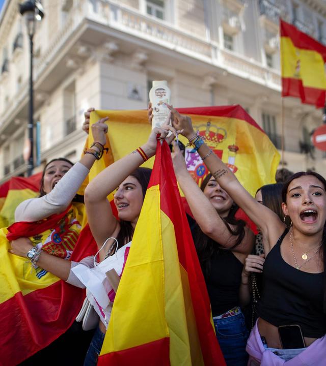 Menschen halten spanische Flaggen hoch und skandieren Parolen.