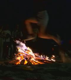 Ein junger Mann springt durch ein Feuer am Strand in Spanien. 