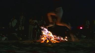 Ein junger Mann springt durch ein Feuer am Strand in Spanien. 
