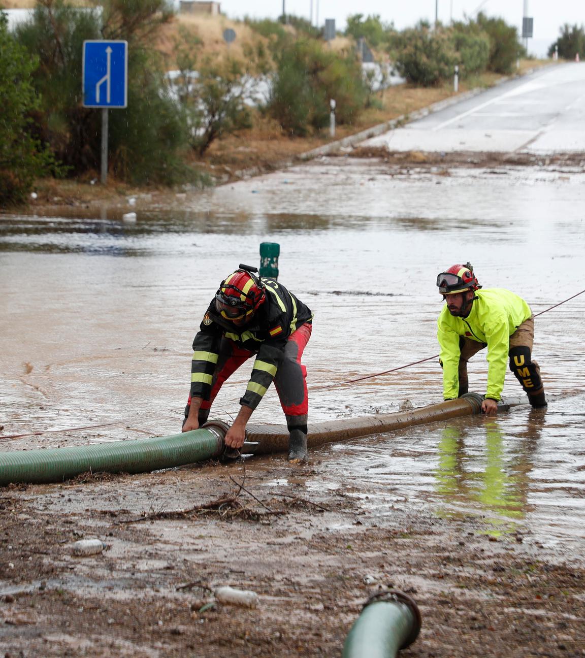 Vier Rettungskräfte stehen in Grisen im Nordosten von Spanien auf einer überfluteten Straße.