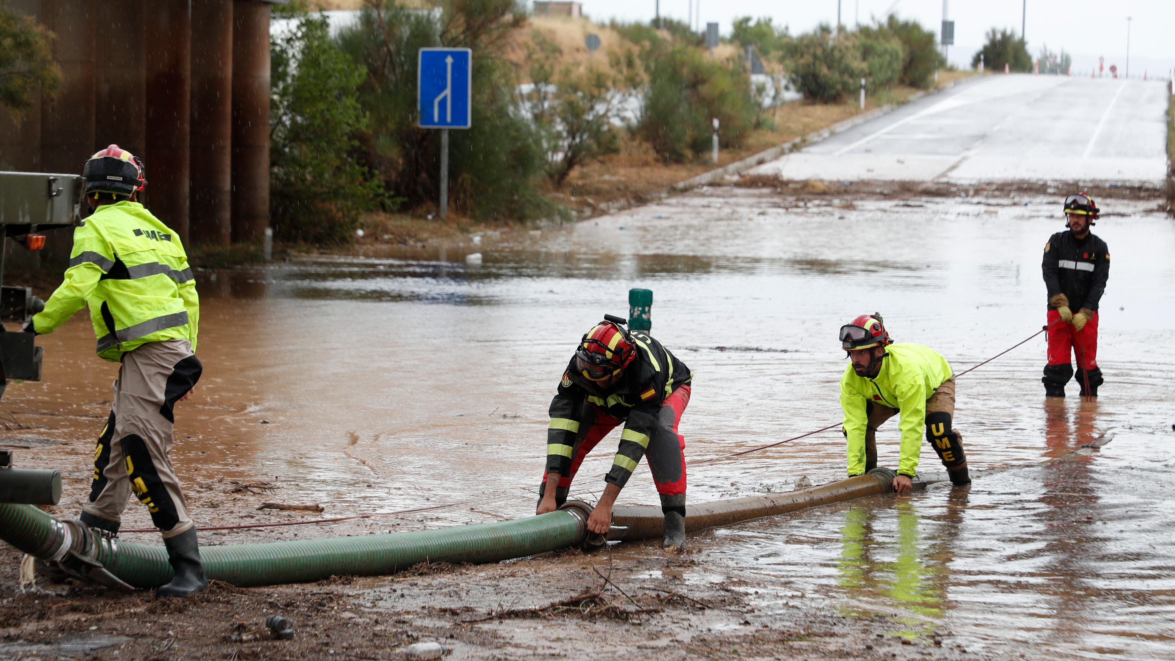 Vier Rettungskräfte stehen in Grisen im Nordosten von Spanien auf einer überfluteten Straße.