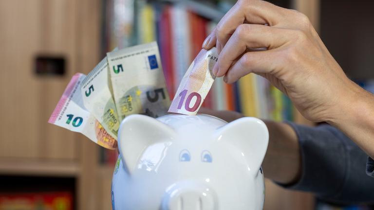 ine Frau steckt einen 10-Euro-Schein in ein Sparschwein. 