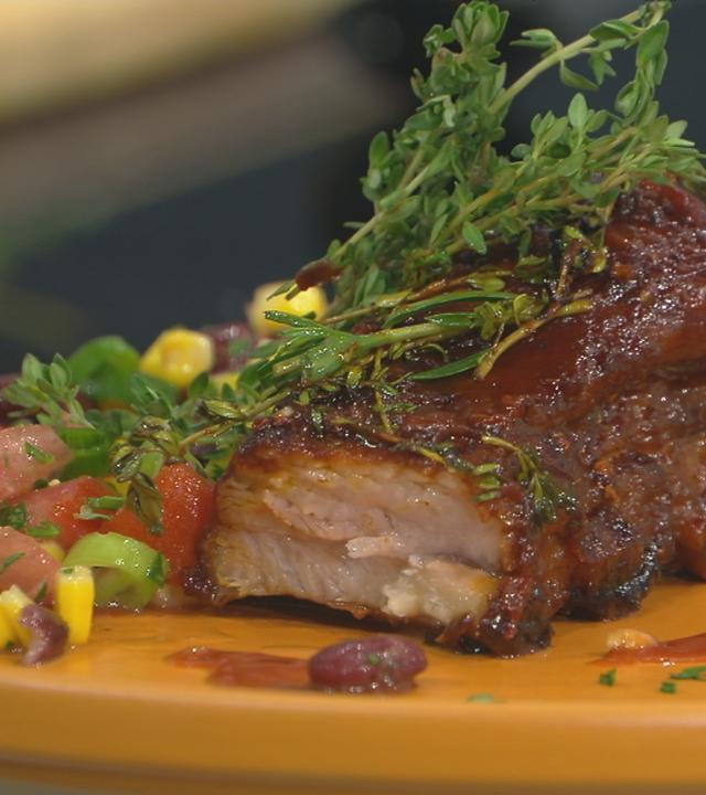 Spareribs mit Barbecue-Sauce und einem Mais-Bohnen-Salat auf einem Teller serviert.