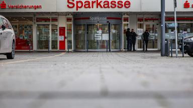 Security-Mitarbeiter sprechen vor der nach einem Einbruch weiterhin geschlossenen Filiale der Sparkasse Gelsenkirchen mit einer Frau