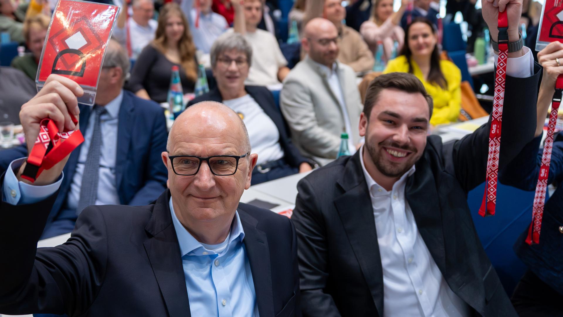 Dietmar Woidke (l, SPD), Ministerpräsident von Brandenburg, und Kurt Fischer (r), Generalsekretär der SPD-Brandenburg, halten während des Brandenburger SPD-Landesparteitages bei der Abstimmung über den Koalitionsvertrag zwischen SPD und CDU die roten Stimmkarten hoch.