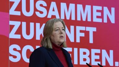 Bärbel Bas spricht zu den Anwesenden der Jahresauftaktsversammlung der SPD. Sie steht vor einem roten Hintergrund auf dem die Worte "Zusammen Zukunft schreiben" stehen.