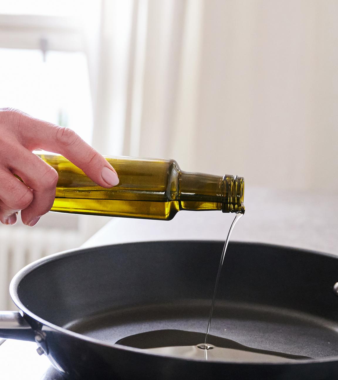 Frau gießt Öl aus einer Flasche in eine Pfanne