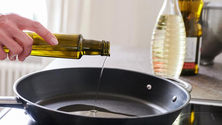 Frau gießt Öl aus einer Flasche in eine Pfanne
