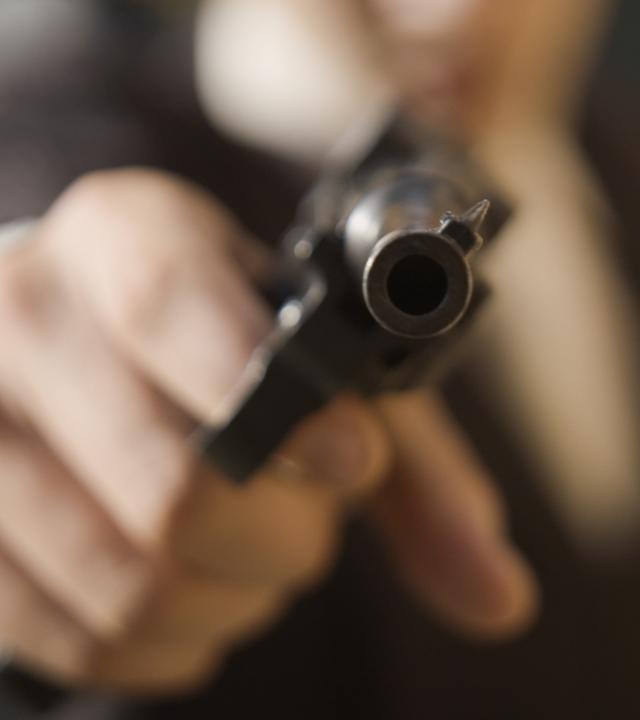 Eine Person zielt mit einer Pistole direkt in die Kamera.