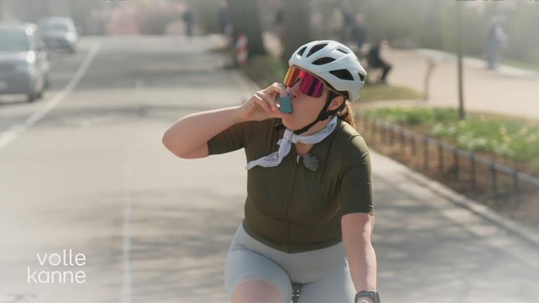 Frau fährt Rennrad und nutzt ein Asthmaspray.