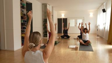 Eine Gruppe an Menschen sitzt auf Yogamatten und macht Yoga Übungen
