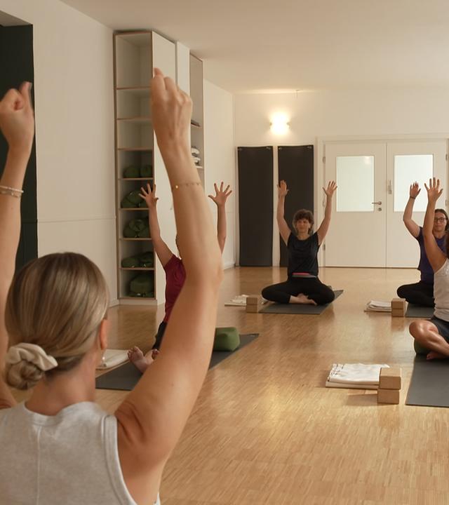 Eine Gruppe an Menschen sitzt auf Yogamatten und macht Yoga Übungen
