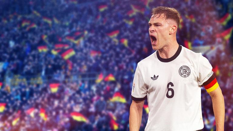 Nationalspieler und Kaptitän Josuah Kimmich in einem Fußballstadion mit Fans, von denen einige Deutschlandfahnen auf den Tribünen schwenken