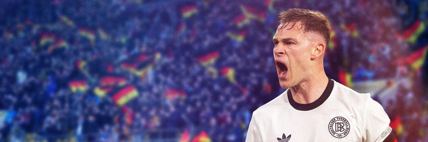 Nationalspieler und Kaptitän Josuah Kimmich in einem Fußballstadion mit Fans, von denen einige Deutschlandfahnen auf den Tribünen schwenken