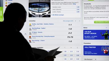Ein Mann steht vor einem Bildschirm mit einer Seite eines Anbieters für Sport-Wetten