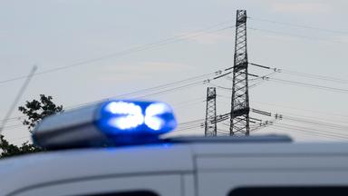 Ein Polizeiauto ist vor einer Hochspannungsleitung zu sehen.