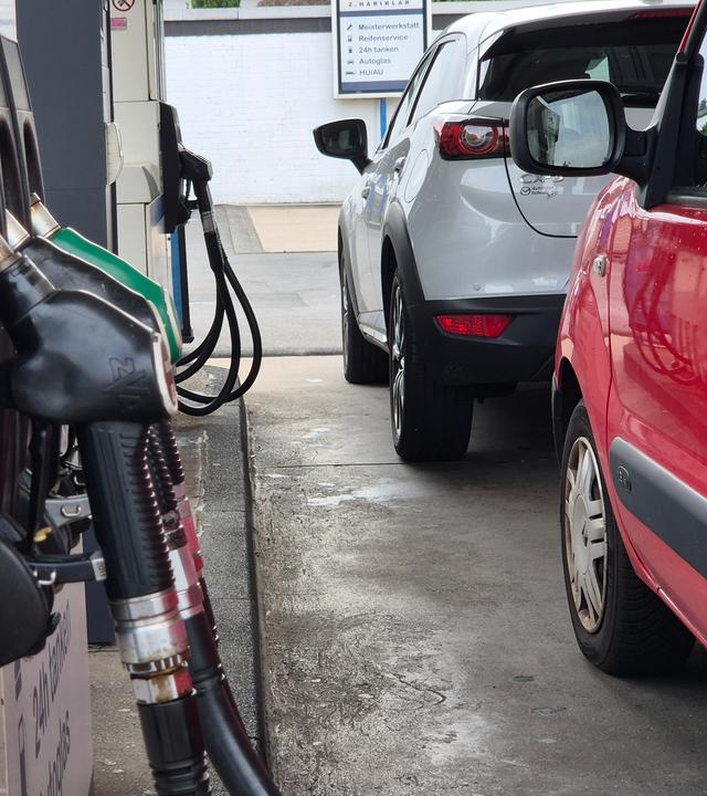Zwei Autos stehen neben einer Zapfsäule an der Tankstelle.