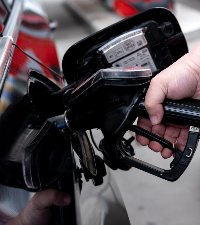 Bayern, München: Ein Mann hält eine Zapfpistole an einer Tankstelle in der Hand und betankt sein Auto.
