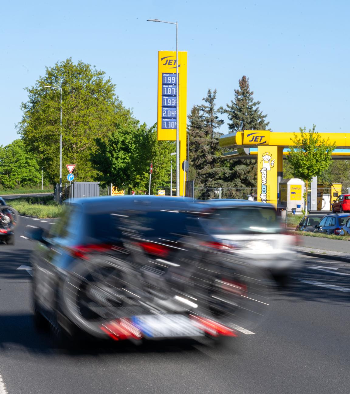 Bayern, Bamberg: An einer Tankstelle in Bamberg stehen Autos an den Zapfsäulen zum Tanken, während weitere Fahrzeuge mit Gepäckträgern und Fahrrädern bei bestem Ausflugswetter auf einer Straße davor vorbeifahren.