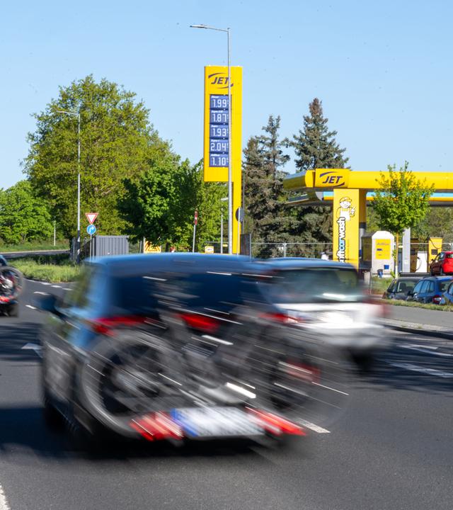 Bayern, Bamberg: An einer Tankstelle in Bamberg stehen Autos an den Zapfsäulen zum Tanken, während weitere Fahrzeuge mit Gepäckträgern und Fahrrädern bei bestem Ausflugswetter auf einer Straße davor vorbeifahren.