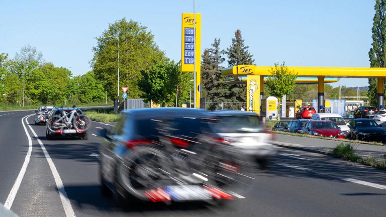 Bayern, Bamberg: An einer Tankstelle in Bamberg stehen Autos an den Zapfsäulen zum Tanken, während weitere Fahrzeuge mit Gepäckträgern und Fahrrädern bei bestem Ausflugswetter auf einer Straße davor vorbeifahren.