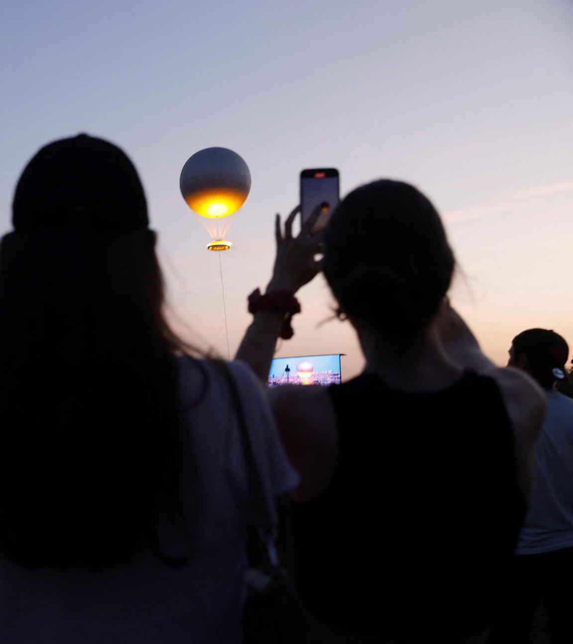 Drei Frauen beobachten, wie die an einem Ballon befestigte olympische Feuerschale bei Sonnenuntergang während des Musikfestes in Paris am 21. Juni 2025 am Himmel schwebt. 