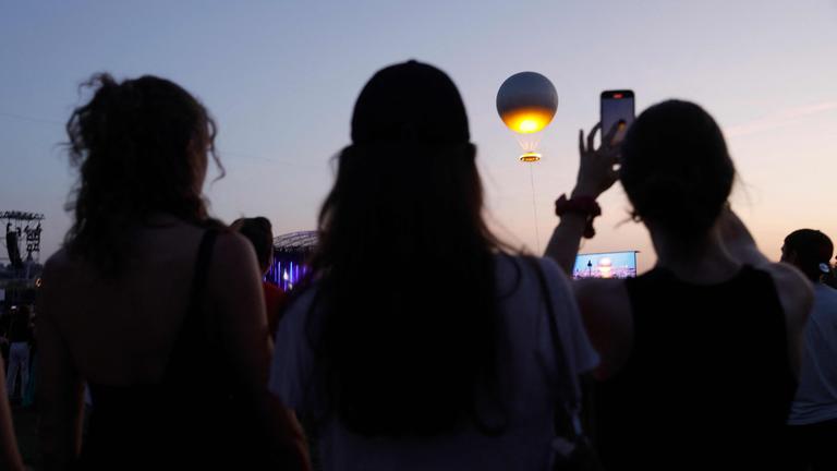 Drei Frauen beobachten, wie die an einem Ballon befestigte olympische Feuerschale bei Sonnenuntergang während des Musikfestes in Paris am 21. Juni 2025 am Himmel schwebt. 