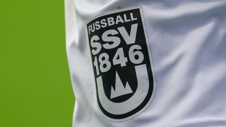 Auf der Hose eines Spielers ist das Logo des SSV Ulm zu sehen. Fußball SSV 1846 steht über einer minimalistischen Münster-Abbildung, welche von einem U umrandet wird.