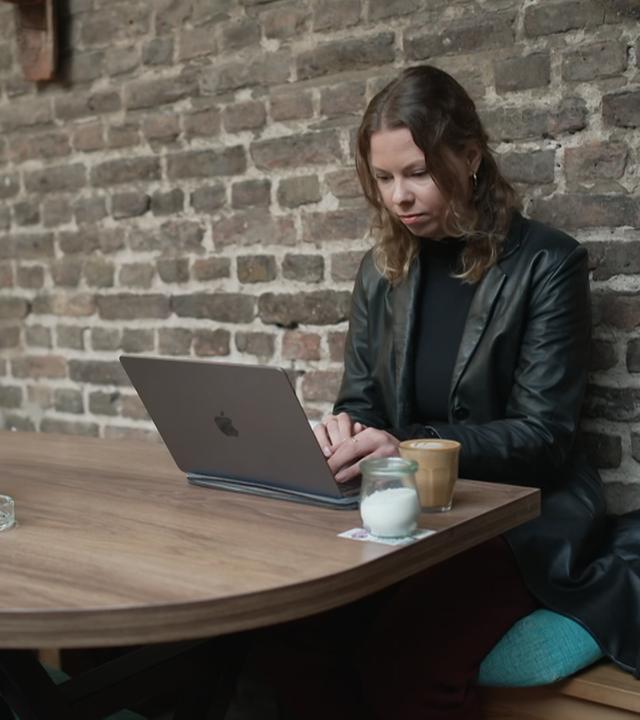 Eine Frau sitzt mit einem Laptop in einem Cafe. 