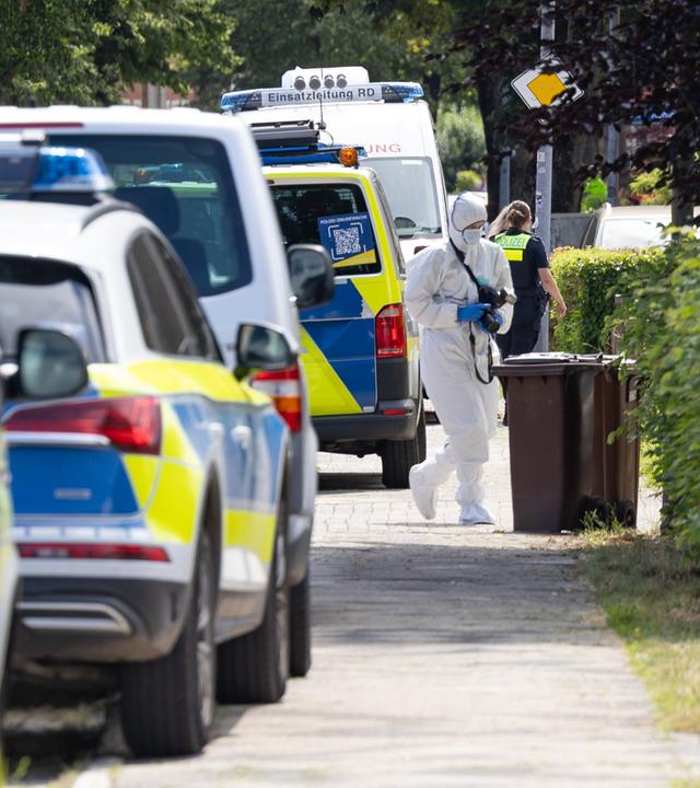 Einsatzkräfte der Spurensicherung stehen auf einer Straße in Stade, daneben Polizeiautos.