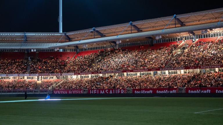  Die Tribünen des Max-Morlock-Stadions sind bis auf den letzten Platz gefüllt. Tausende Besucher:innen sitzen mit Kerzen in der Hand und schaffen gemeinsam ein beeindruckendes Lichtermeer beim Großen Nürnberger Rote Engel Adventssingen. 