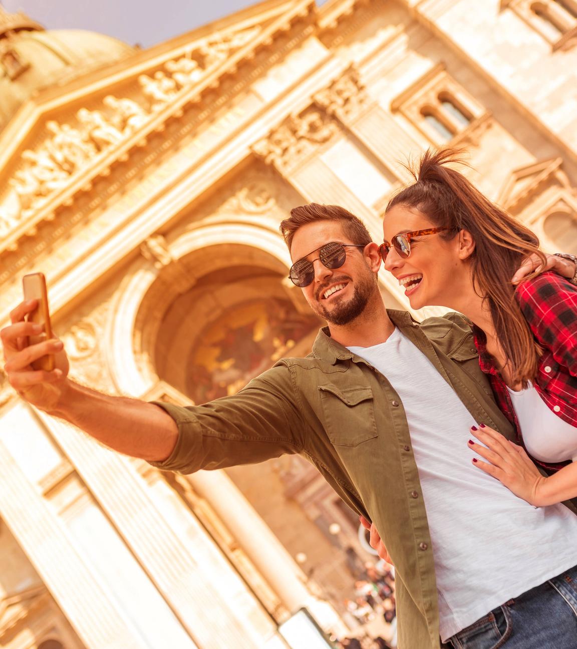 Junges Paar auf einem Städtetrip fortografiert sich vor einem Gebäude.