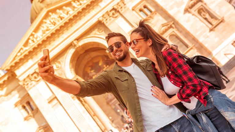 Junges Paar auf einem Städtetrip fortografiert sich vor einem Gebäude.
