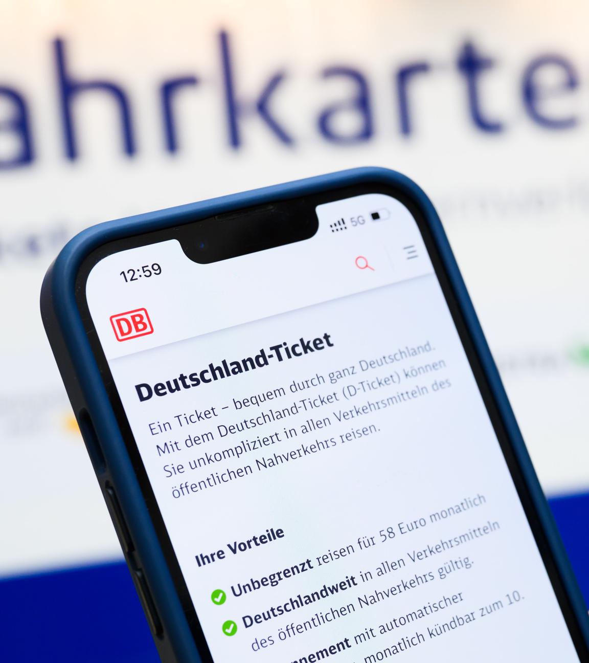 Eine Person hält am Hauptbahnhof ein Smartphone in der Hand, auf dessen Display eine Information zum Kauf des Deutschlandtickets zu sehen ist, während sie vor einem Fahrkartenautomaten steht. 